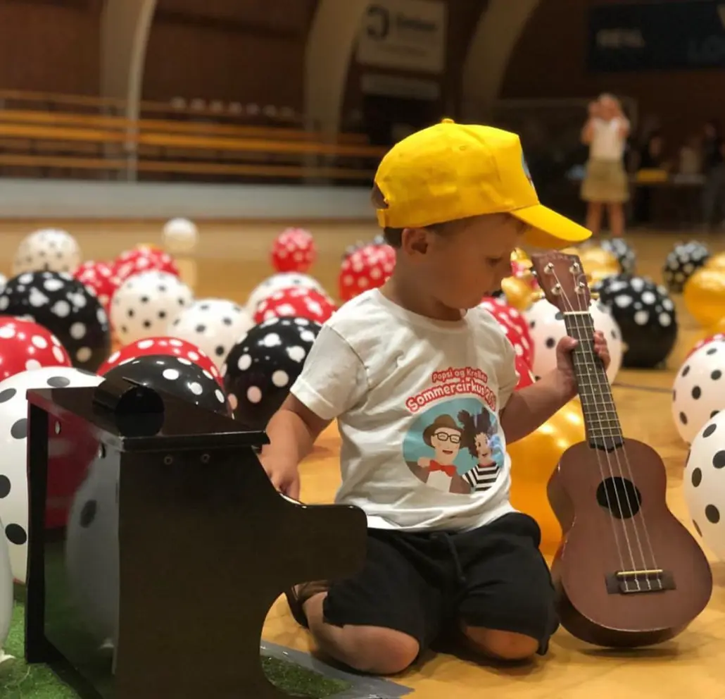 Et barn sidder med en ukulele til et musikarrangement