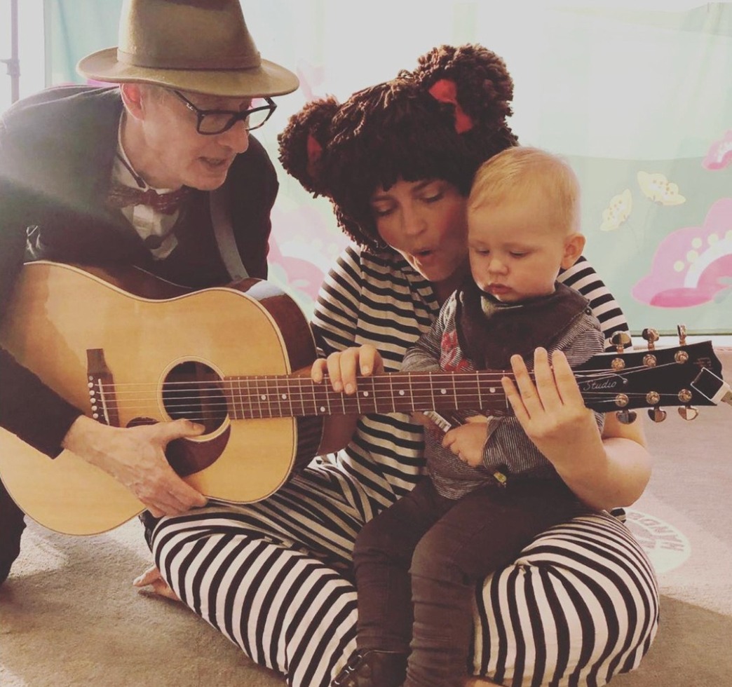 Tre mennesker, heriblandt et lille barn, synger sammen med en guitar